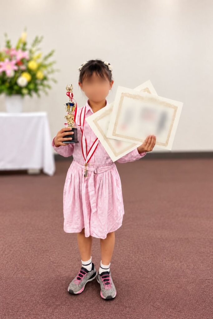 そろばん大会で賞状とトロフィーを持つ子どもの様子